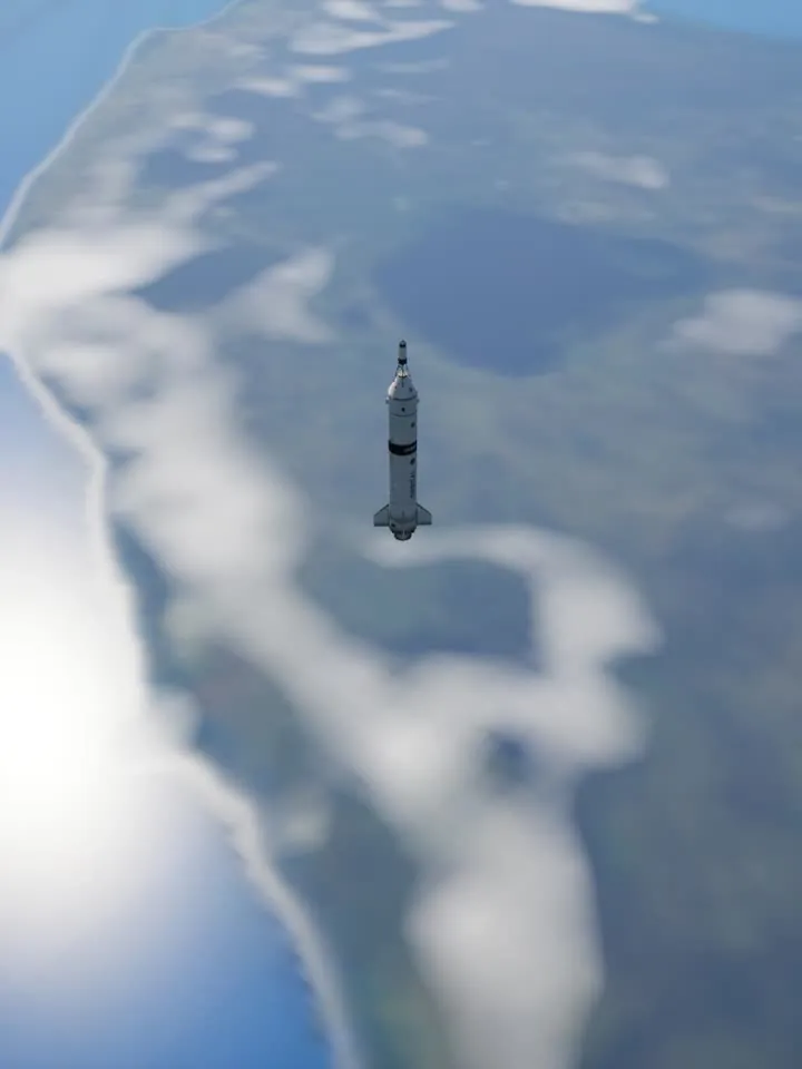 The rocket with its engine off, high above a coastline and clouds.